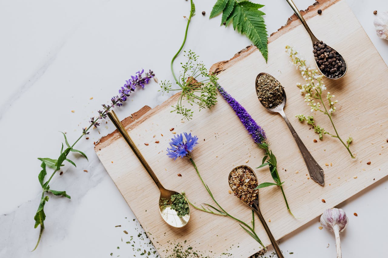 An artistic flat lay of herbs and flowers with teaspoons on a wooden board