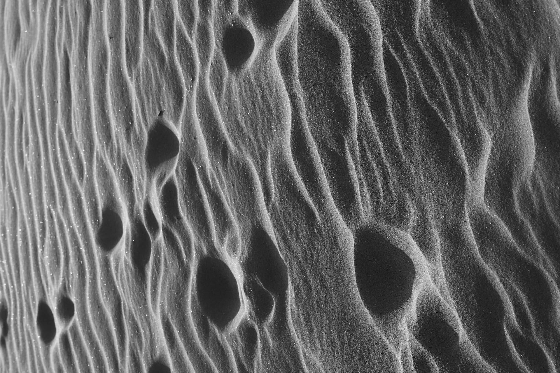 A striking black and white image of sand dunes showing ripples and footprints in an arid landscape